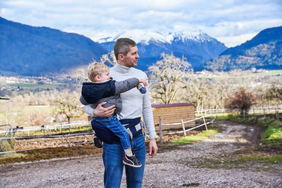 Un homme portant son bébé avec un porte bébé devant les montagnes