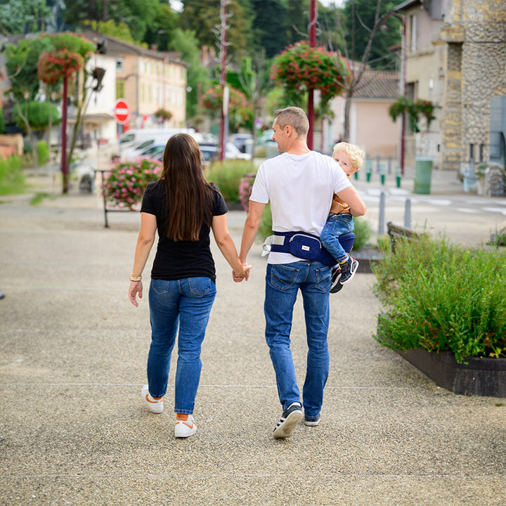 deux jeunes parents portant leur bébé dans la rue avec un porte bébé bleu