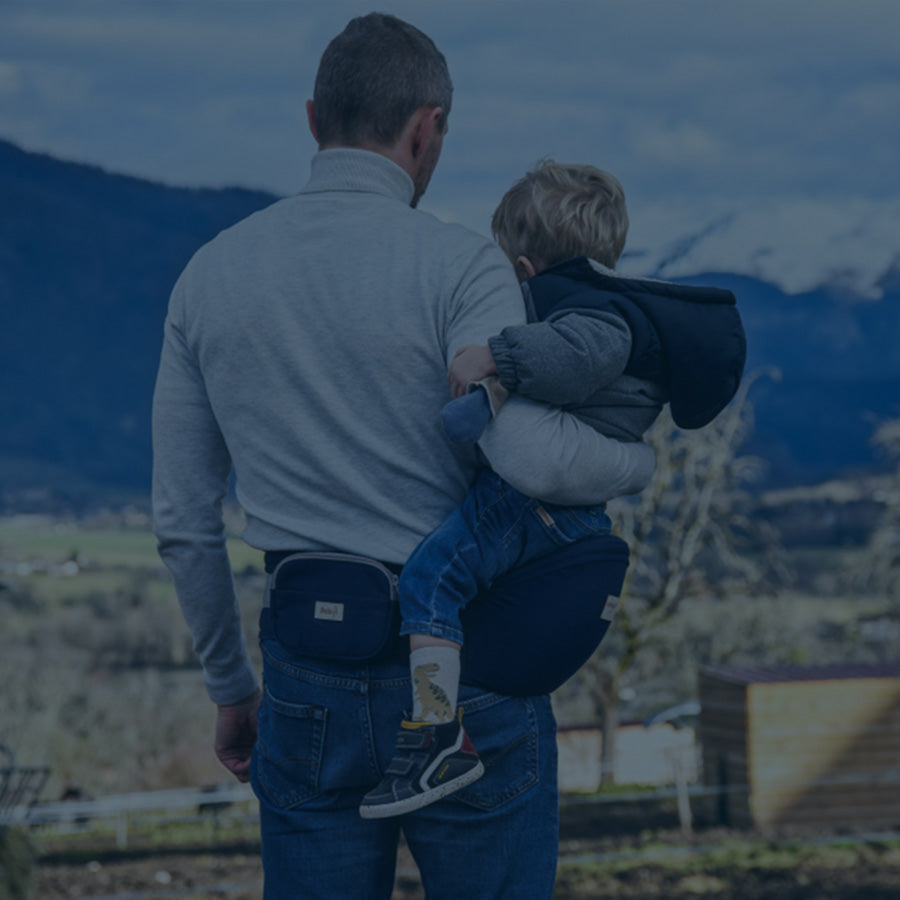 un homme avec un porte bébé bleu et un bébé devant les Alpes