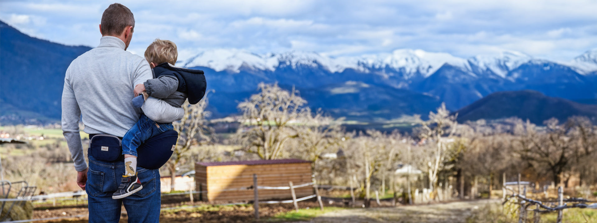 un homme de dos qui porte son bébé devant les montagnes