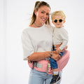 Une femme blonde portant un bébé avec un porte bébé rose