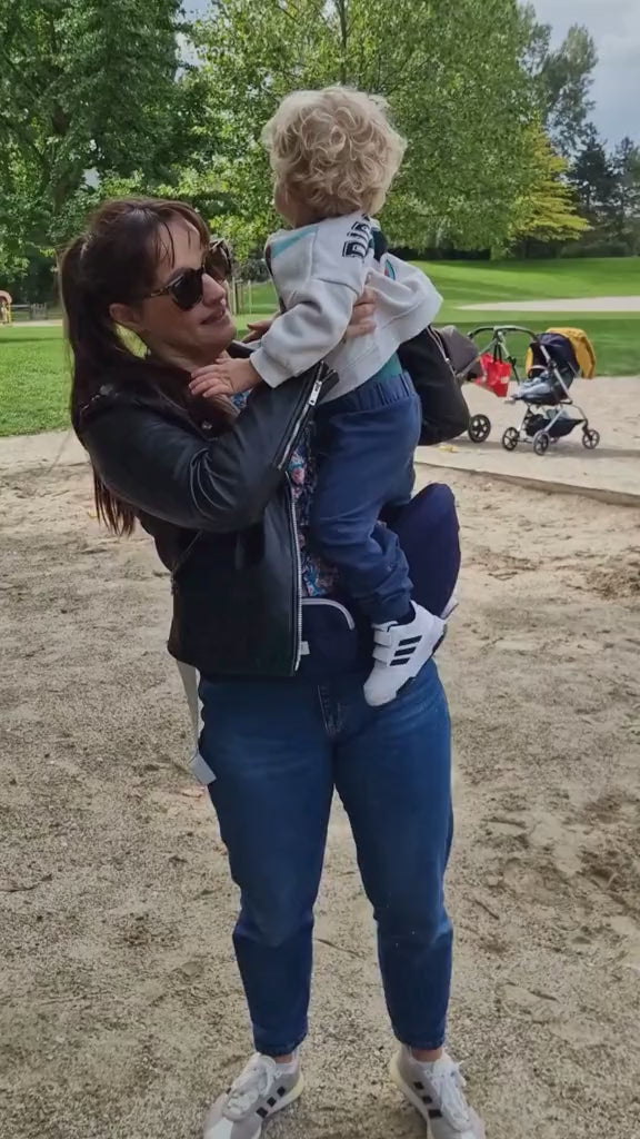 une femme avec un porte bébé bleu dans un parc