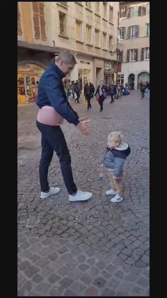 un homme avec un porte bébé rose dans la rue